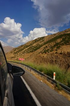 View from car window of a winding road through arid mountains with clear blue skies.