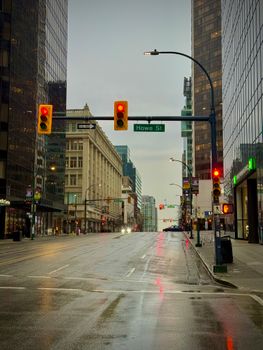 Moody city street in Vancouver with reflections on wet pavement and red traffic lights at Howe St intersection.
