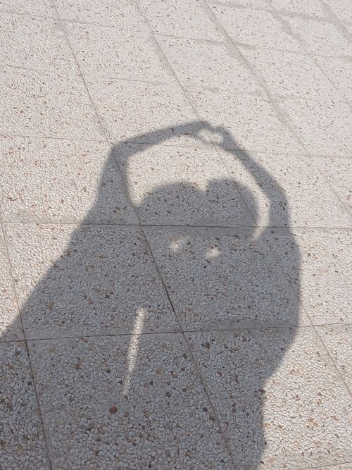 Free A silhouette of a couple forming a heart with their arms on a sunlit pavement. Stock Photo