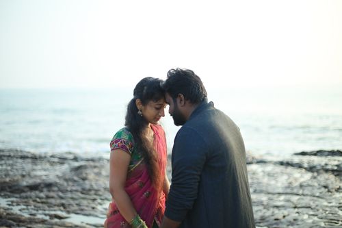 Free Couple sharing a tender moment on a rocky beach with ocean in the background. Stock Photo