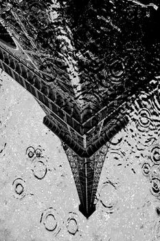 A black and white view of the Eiffel Tower's reflection in a rain-soaked puddle.