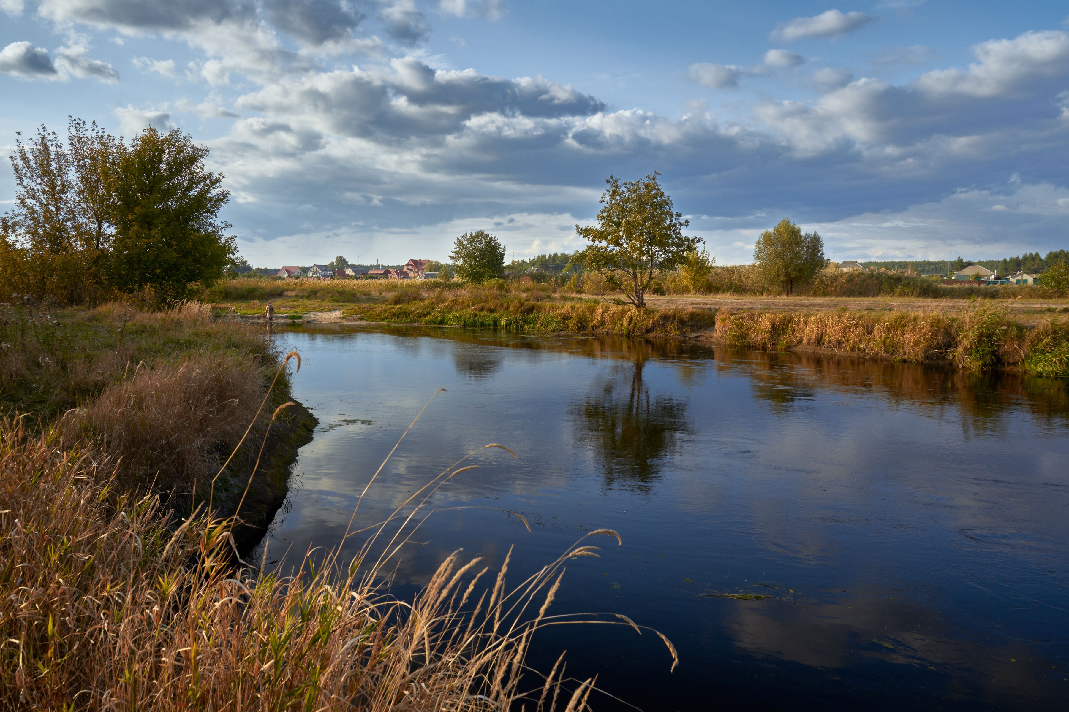 Serene autumn landscape with a calm river and trees under a cloudy sky.