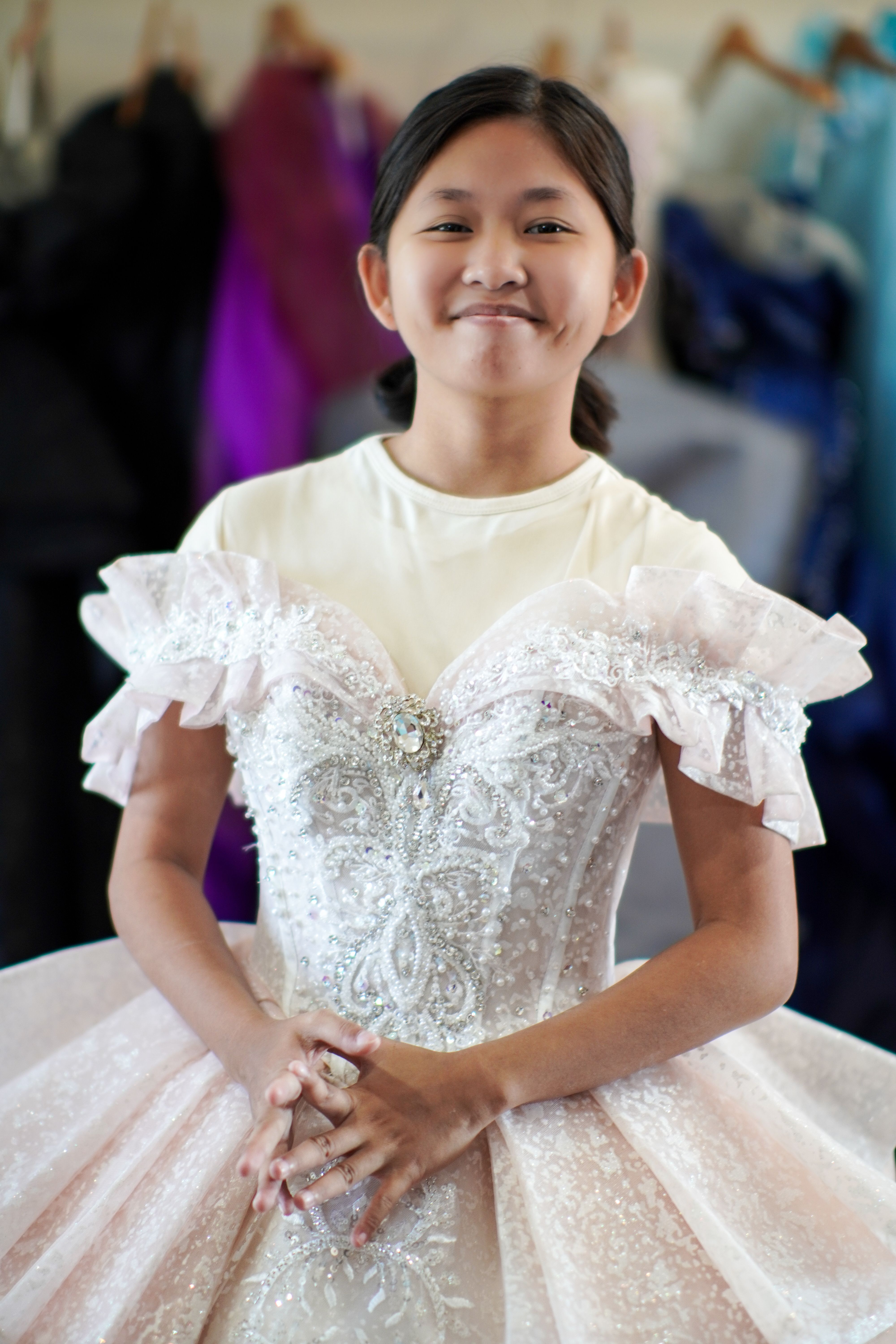 Young girl in a sparkling, intricately detailed white dress, smiling confidently.
