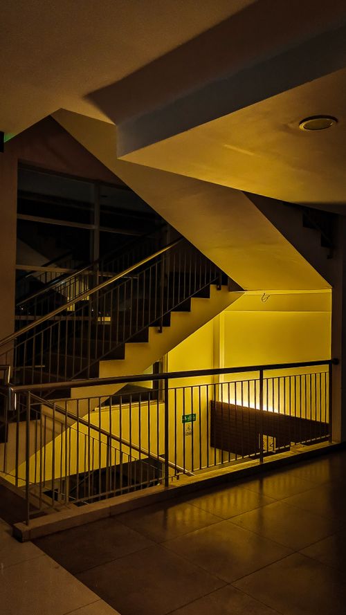 Free A modern staircase with geometric lines illuminated by warm yellow lighting, creating a moody ambiance. Stock Photo