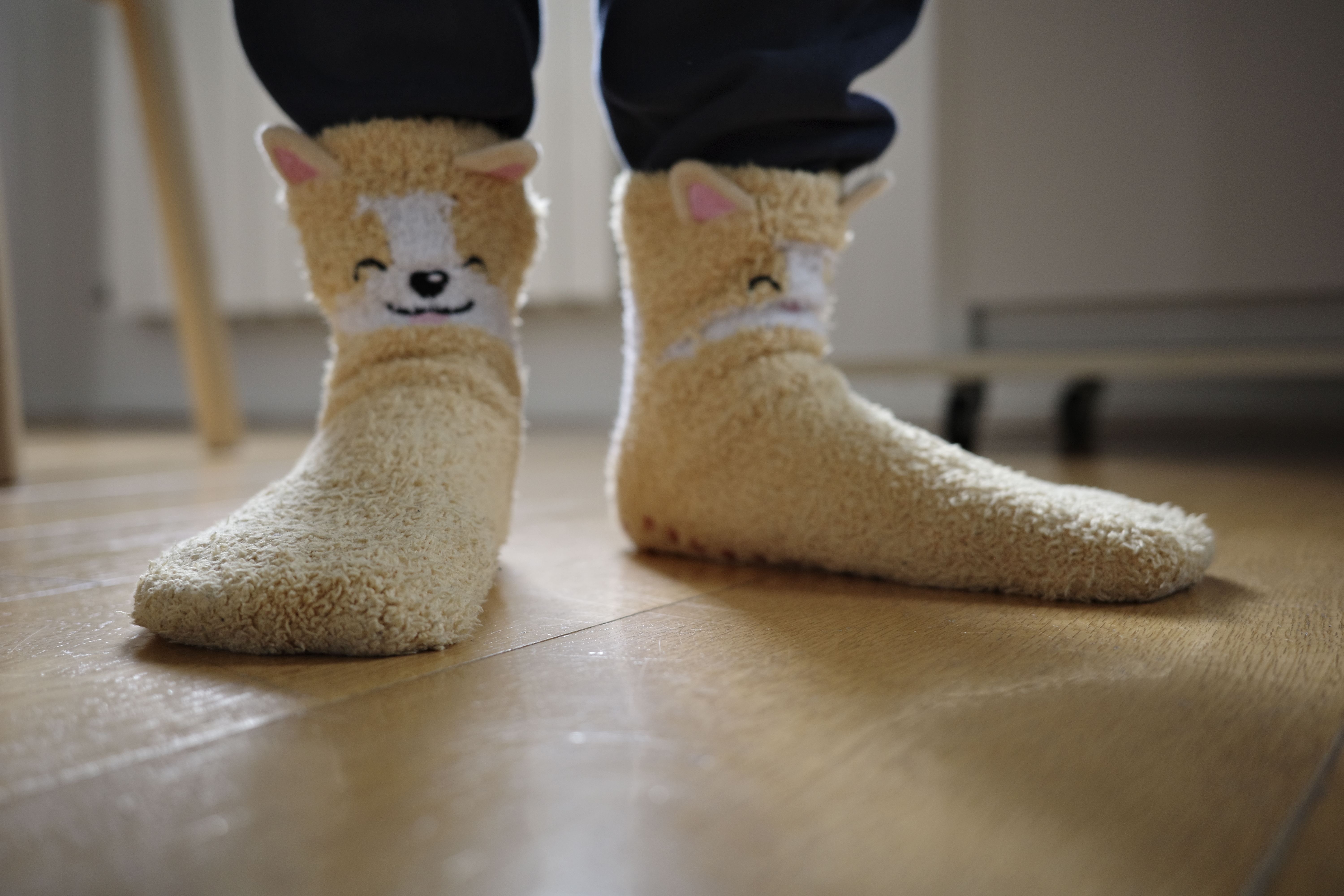 Soft fuzzy socks with cute animal design keep feet warm indoors on a wooden floor.