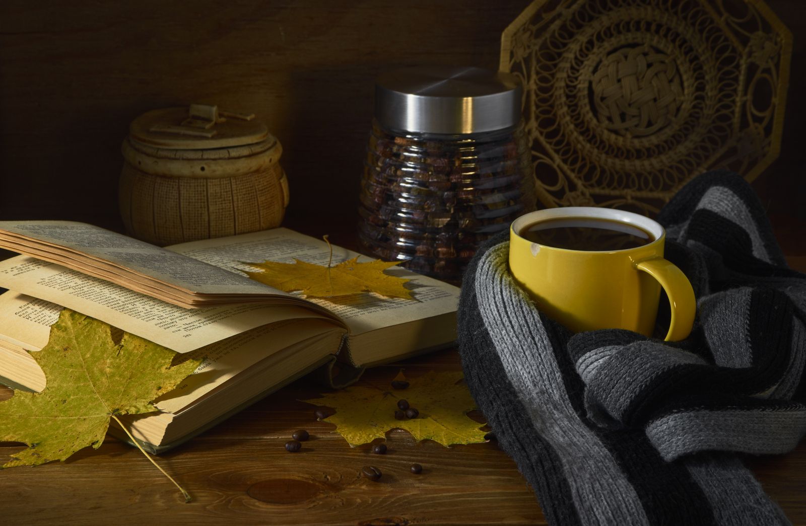 Öppen bok, kaffekopp och höstlöv i varm läsmiljö