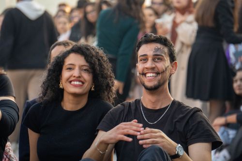 Free Two smiling young adults attending an outdoor event, surrounded by a crowd. Stock Photo