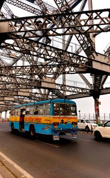 A vibrant local bus crosses the iconic Howrah Bridge, showcasing urban life in Kolkata.