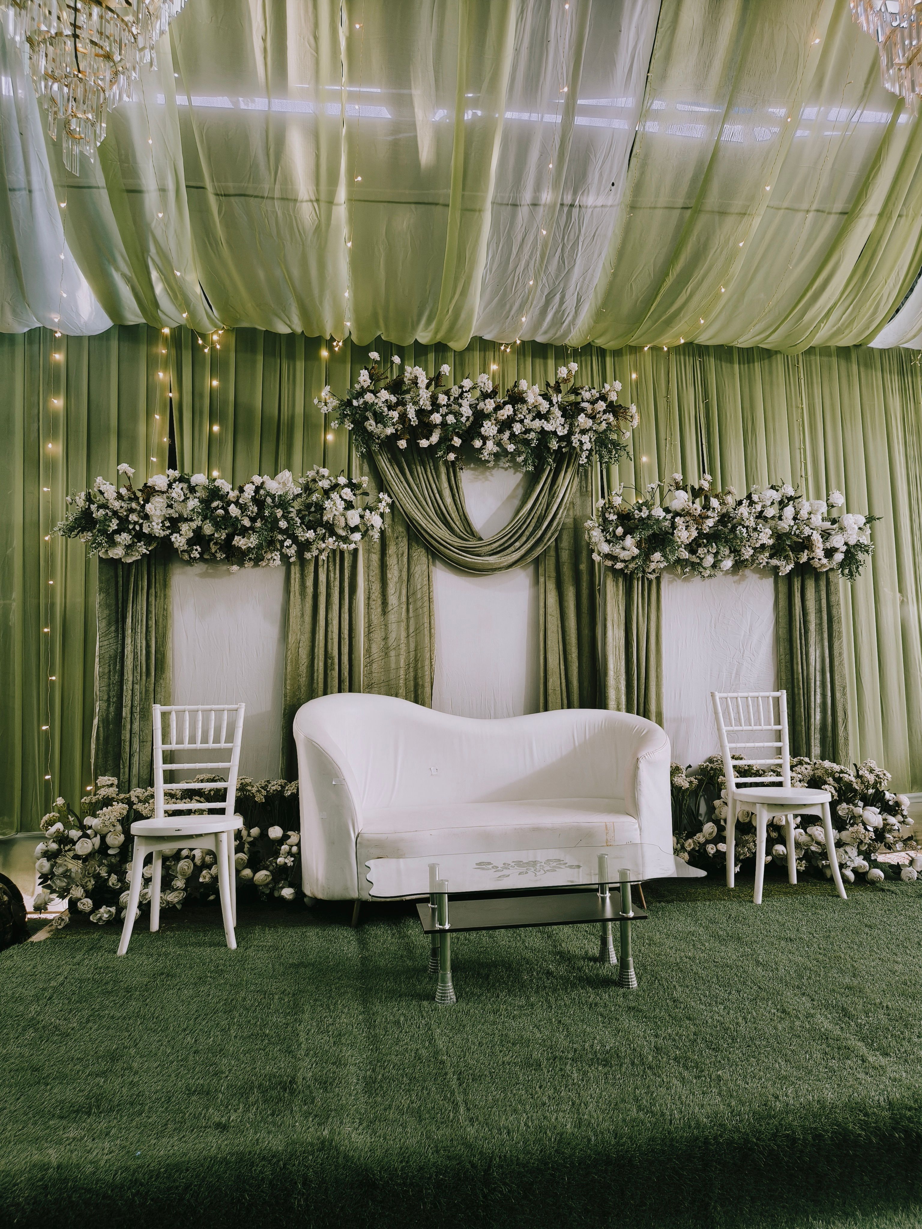 Stylish wedding stage with green drapery and floral decorations, perfect for a modern indoor celebration.