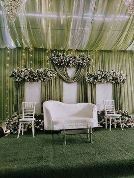 Stylish wedding stage with green drapery and floral decorations, perfect for a modern indoor celebration.