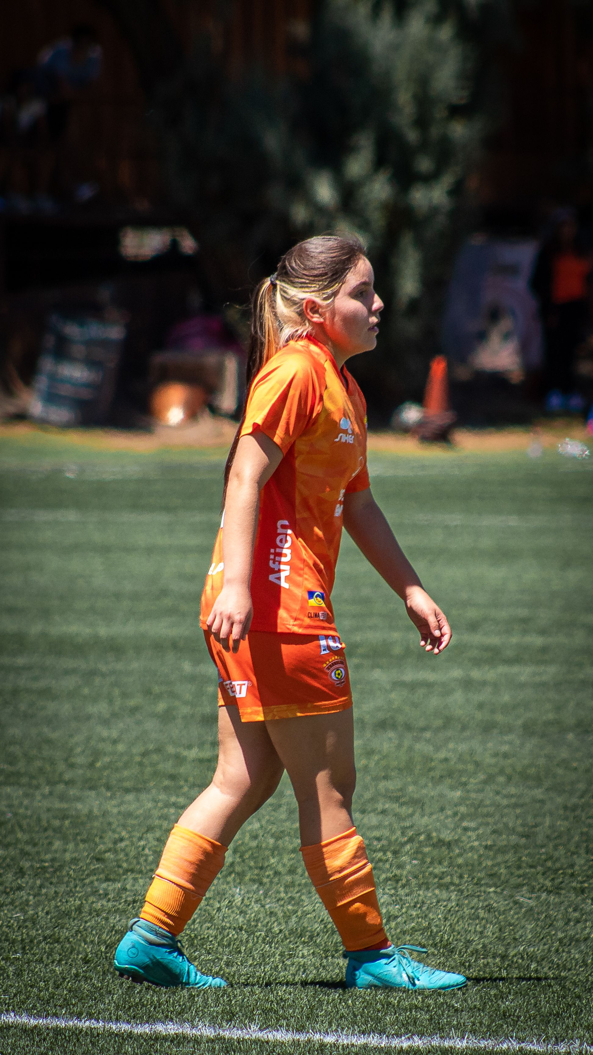 A young woman in an orange soccer uniform on a sunny day on the field.