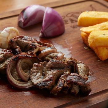 Delicious grilled steak with red onion and fried yuca on a wooden board, offering a savory meal.