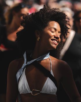 A smiling woman in a white bikini enjoys a sunny outdoor festival.