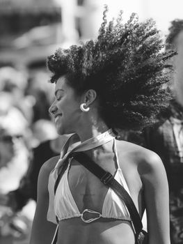 A black and white image of a smiling woman with curly hair and a bikini top embracing a sunny day.