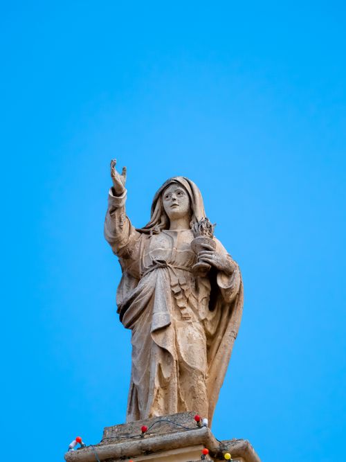 Free A detailed stone statue of a saint reaching upwards, captured against a vibrant blue sky. Stock Photo