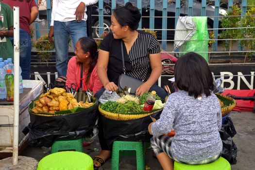 Two women vending various foods in a lively street market setting.