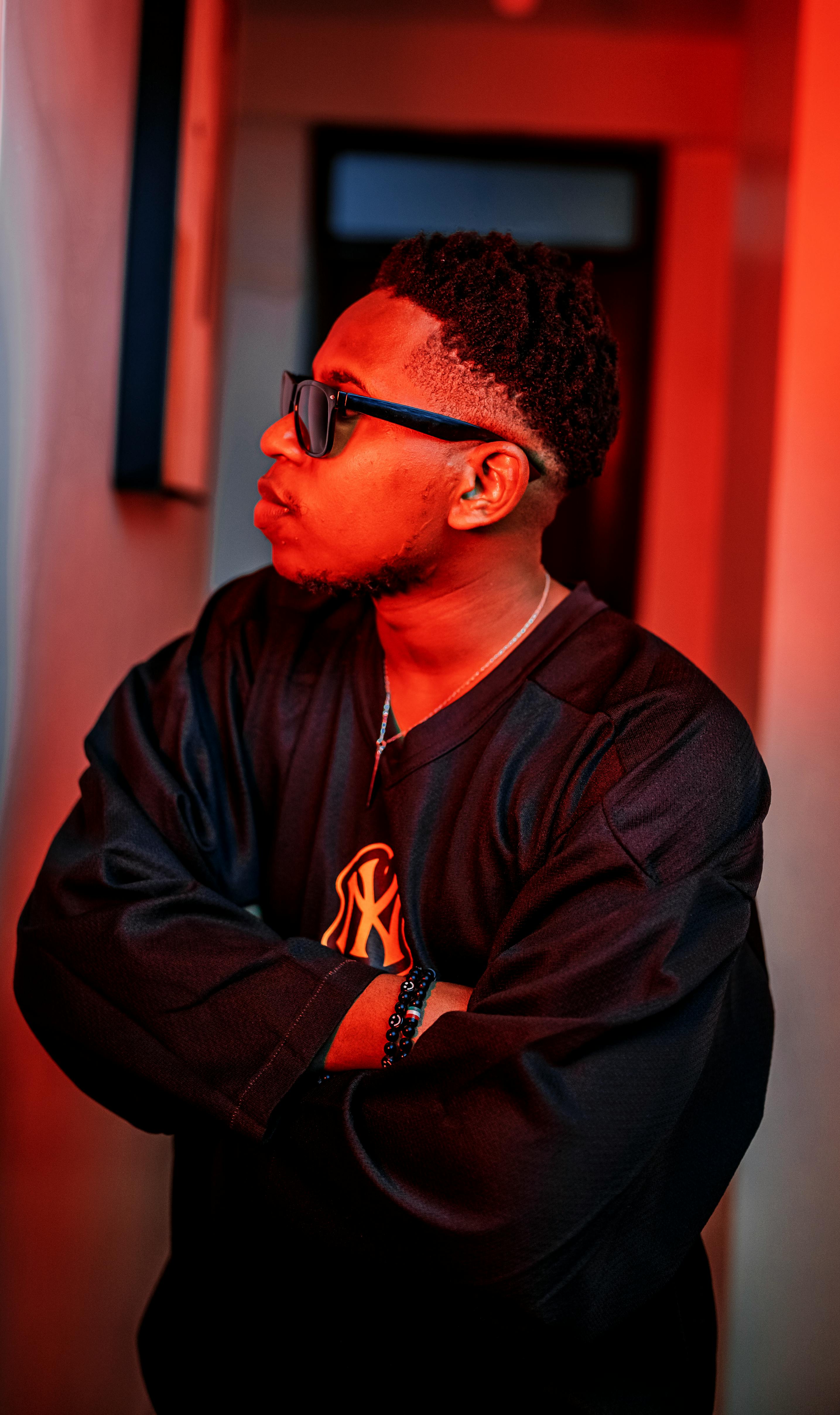 Side profile of an adult man with sunglasses under dramatic red lighting indoors.