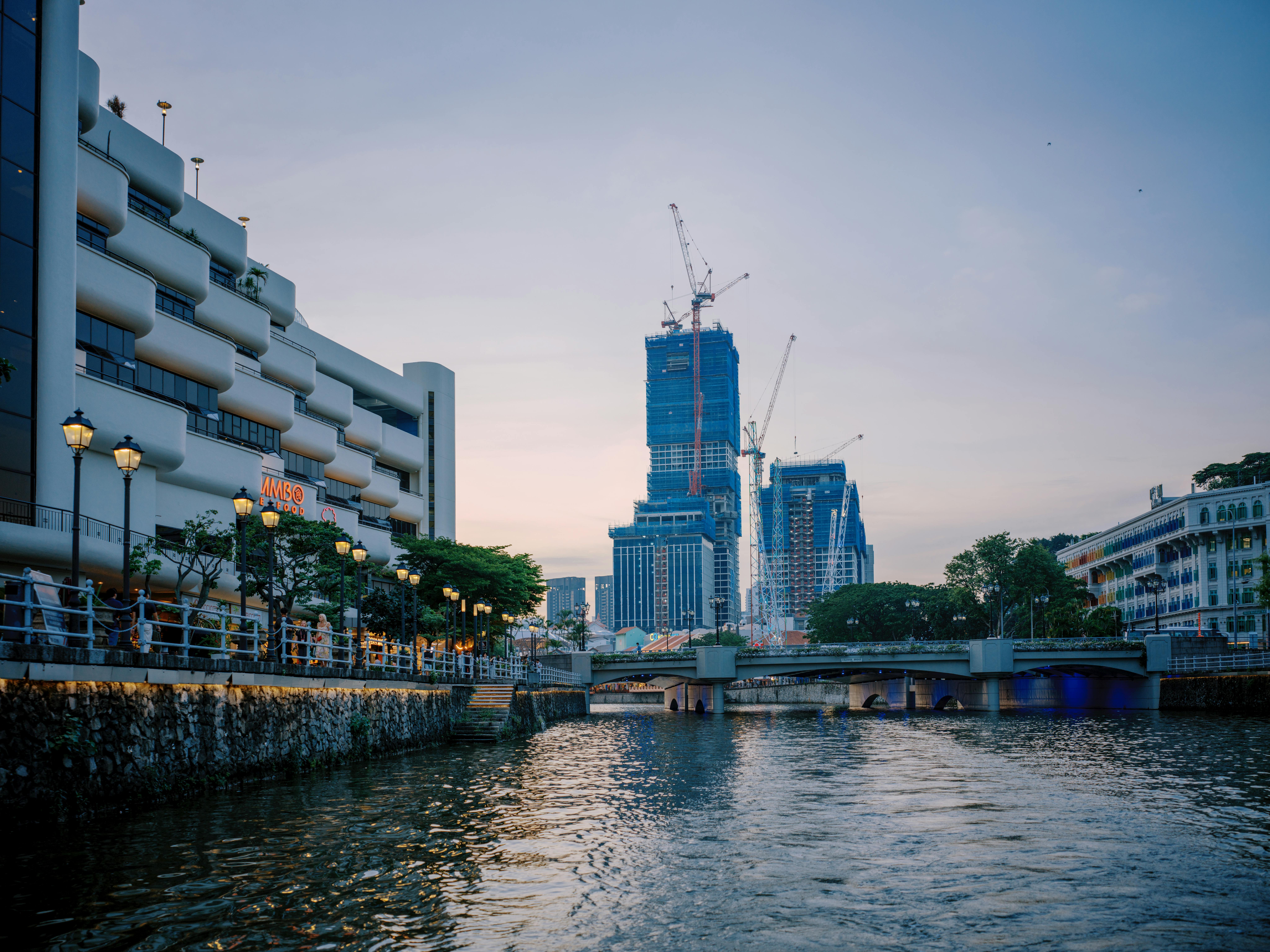 A stunning view of Singapore's riverside skyline with modern architecture and cranes at sunset.