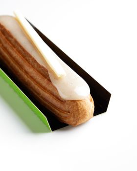 Delicious vanilla glazed eclair with white chocolate decoration in a stylish green holder.