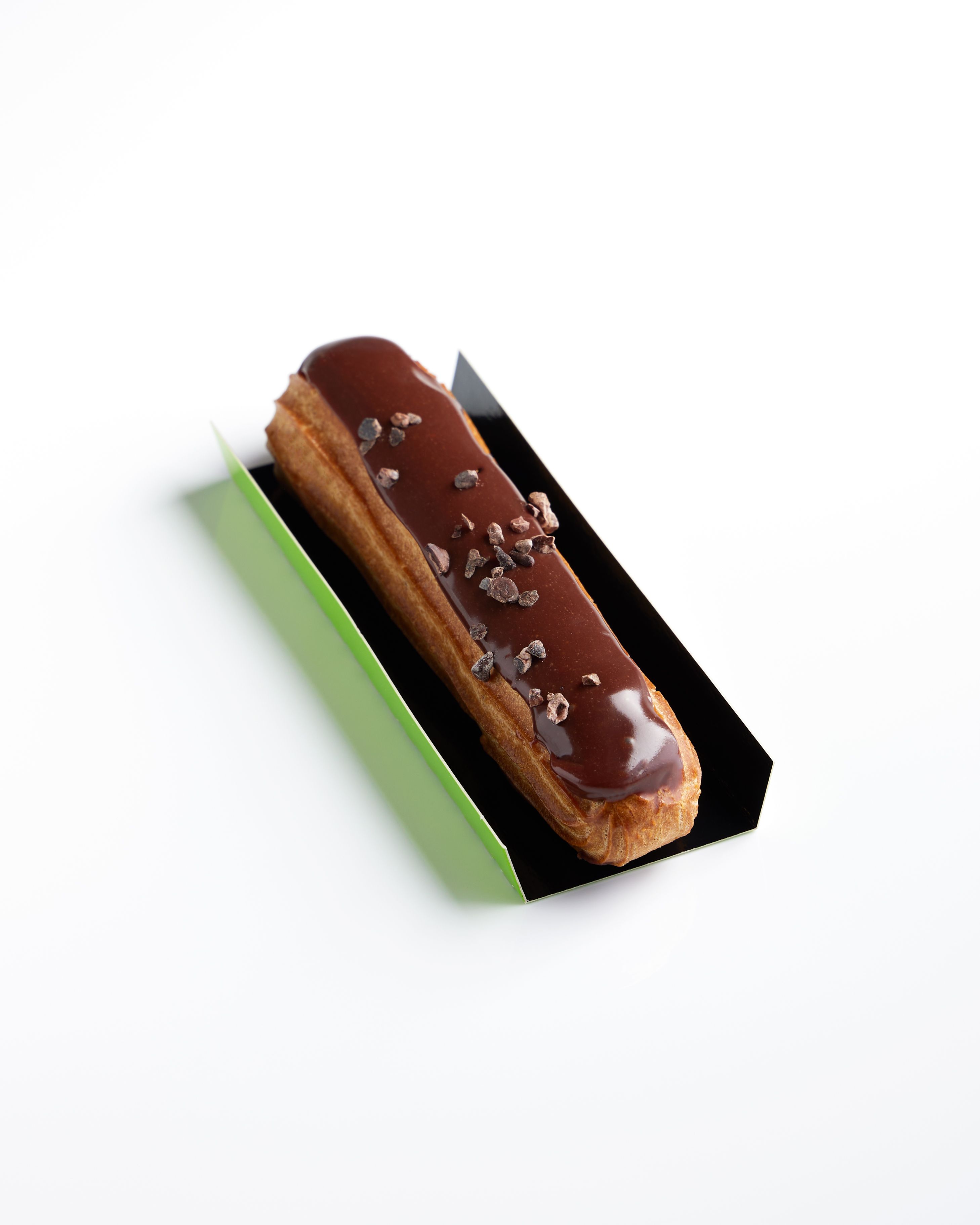 Elegant chocolate eclair with rich glaze and cocoa nibs on a sleek display.