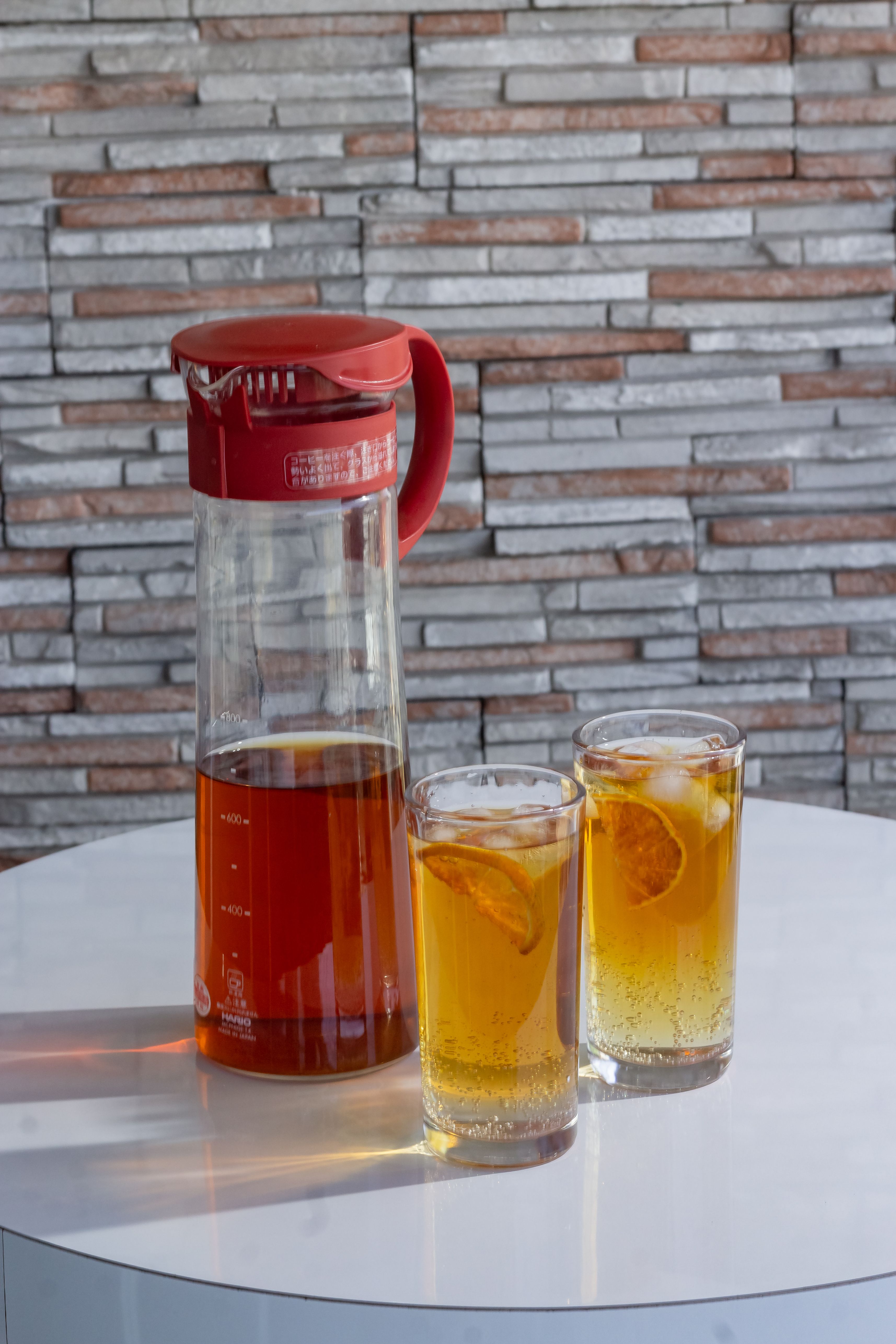 A glass pitcher of homemade iced tea poured over ice on a bright table