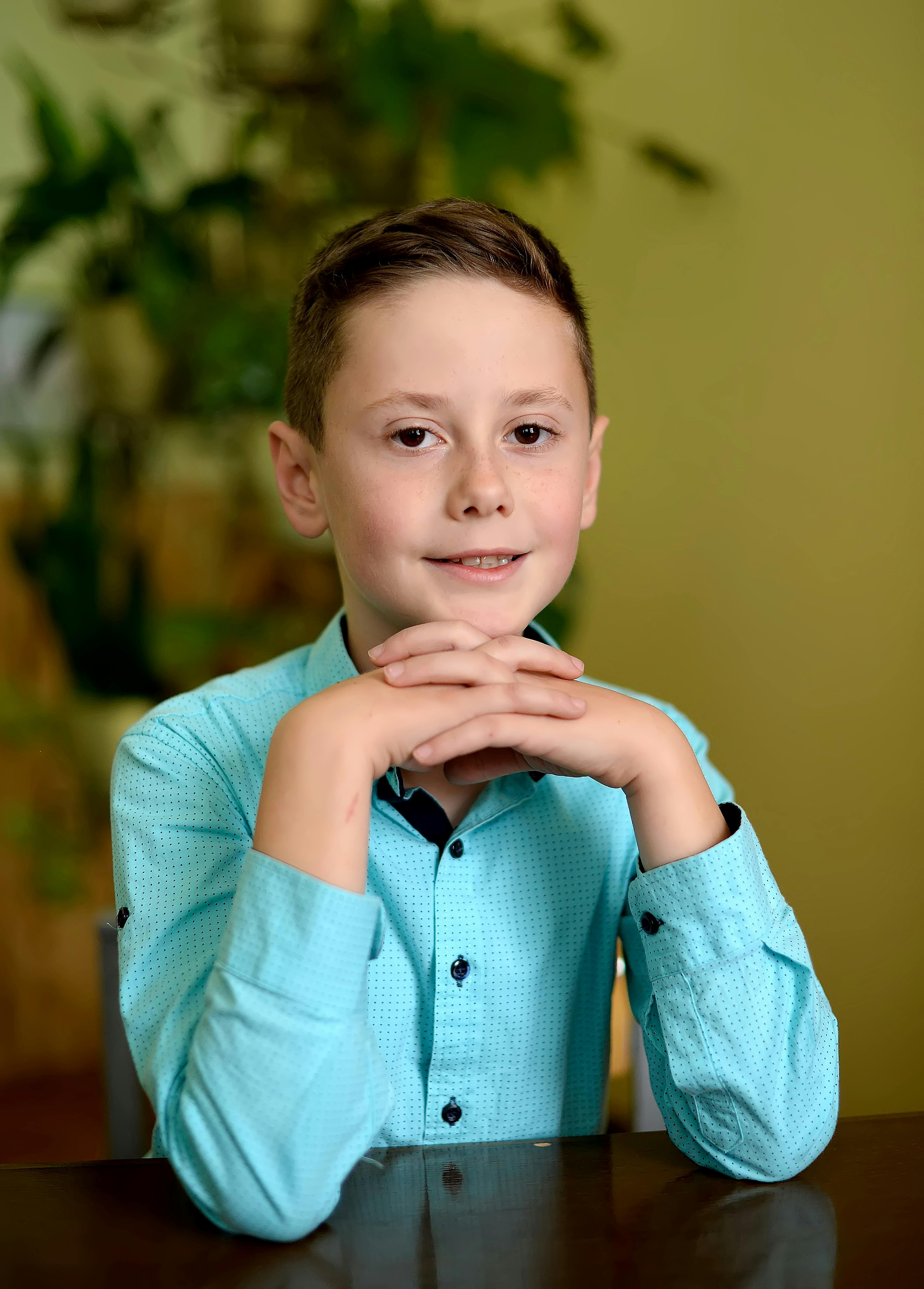 Charming young boy in a turquoise shirt posing indoors with a friendly smile.