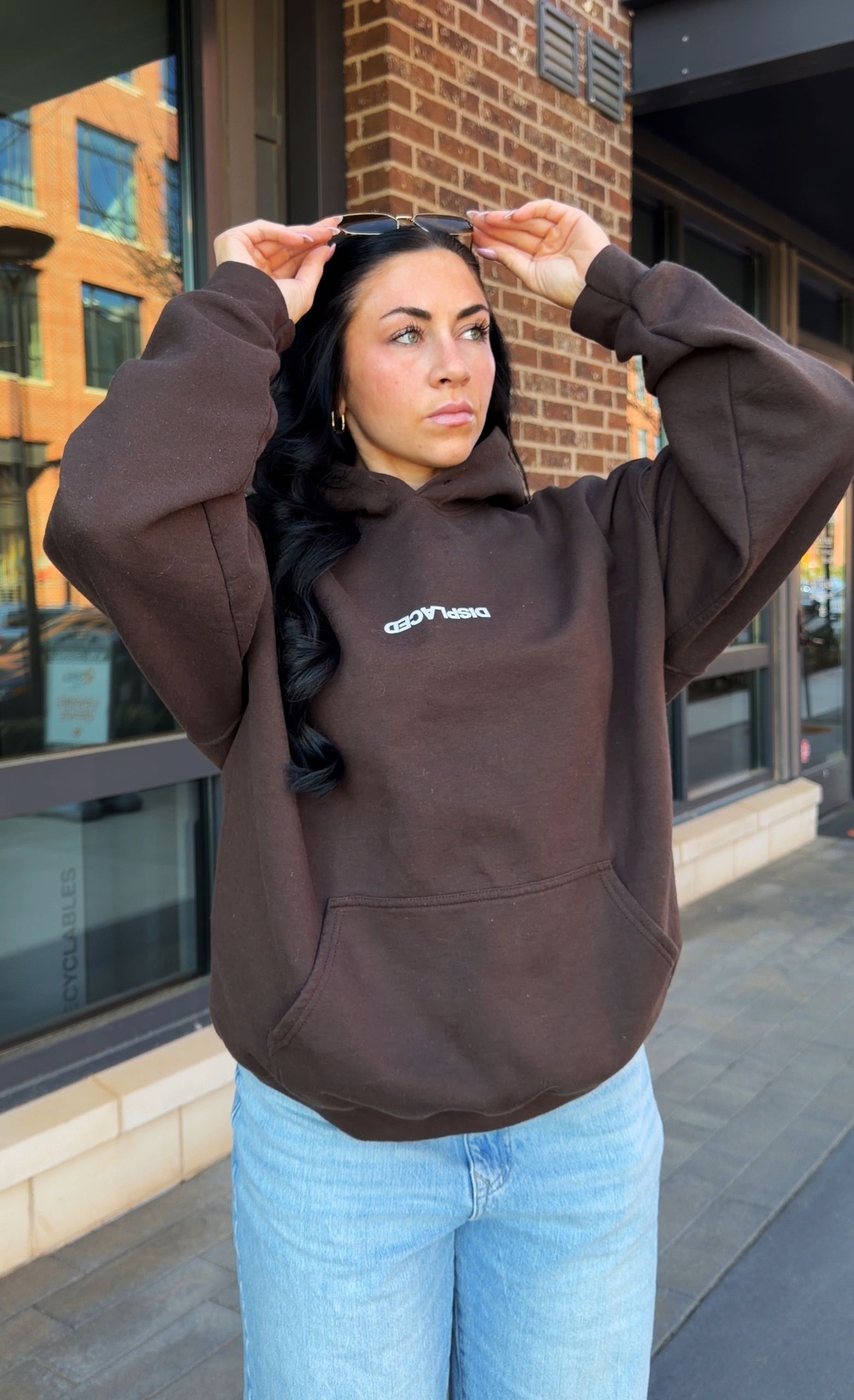 Confident woman posing in a brown hoodie outside a building.