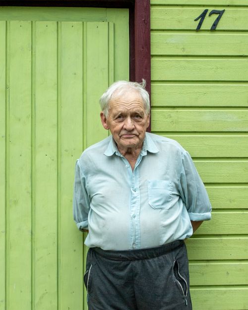 Free Portrait of a senior man against a rustic green wooden house backdrop in Estonia's countryside. Stock Photo
