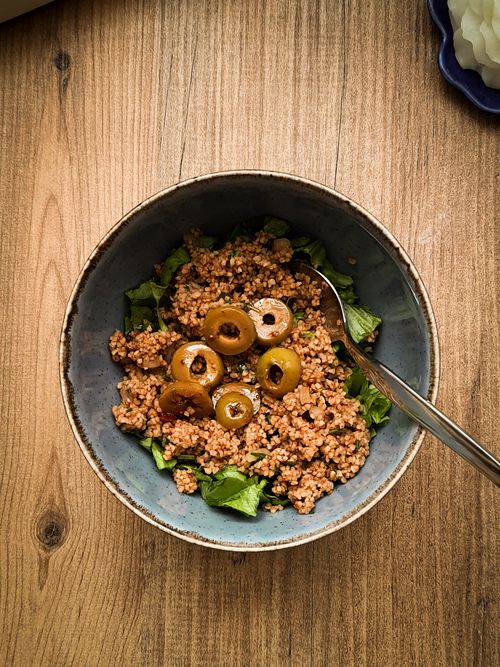 Free Delicious bulgur salad served in a rustic bowl with green olives and herbs on a wooden table. Stock Photo