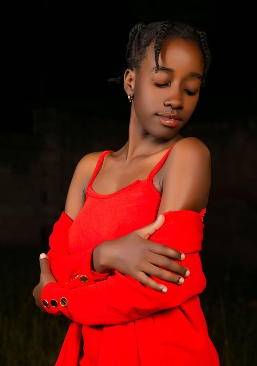 Free A poignant portrait of a young woman embracing herself, wearing a vibrant red dress at night. Stock Photo