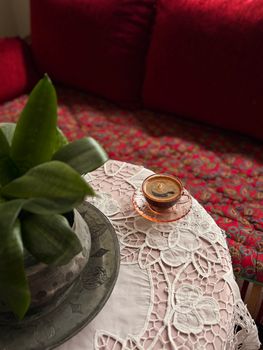 A cozy coffee setup with a plant on a lace-covered table in a red-themed living room.