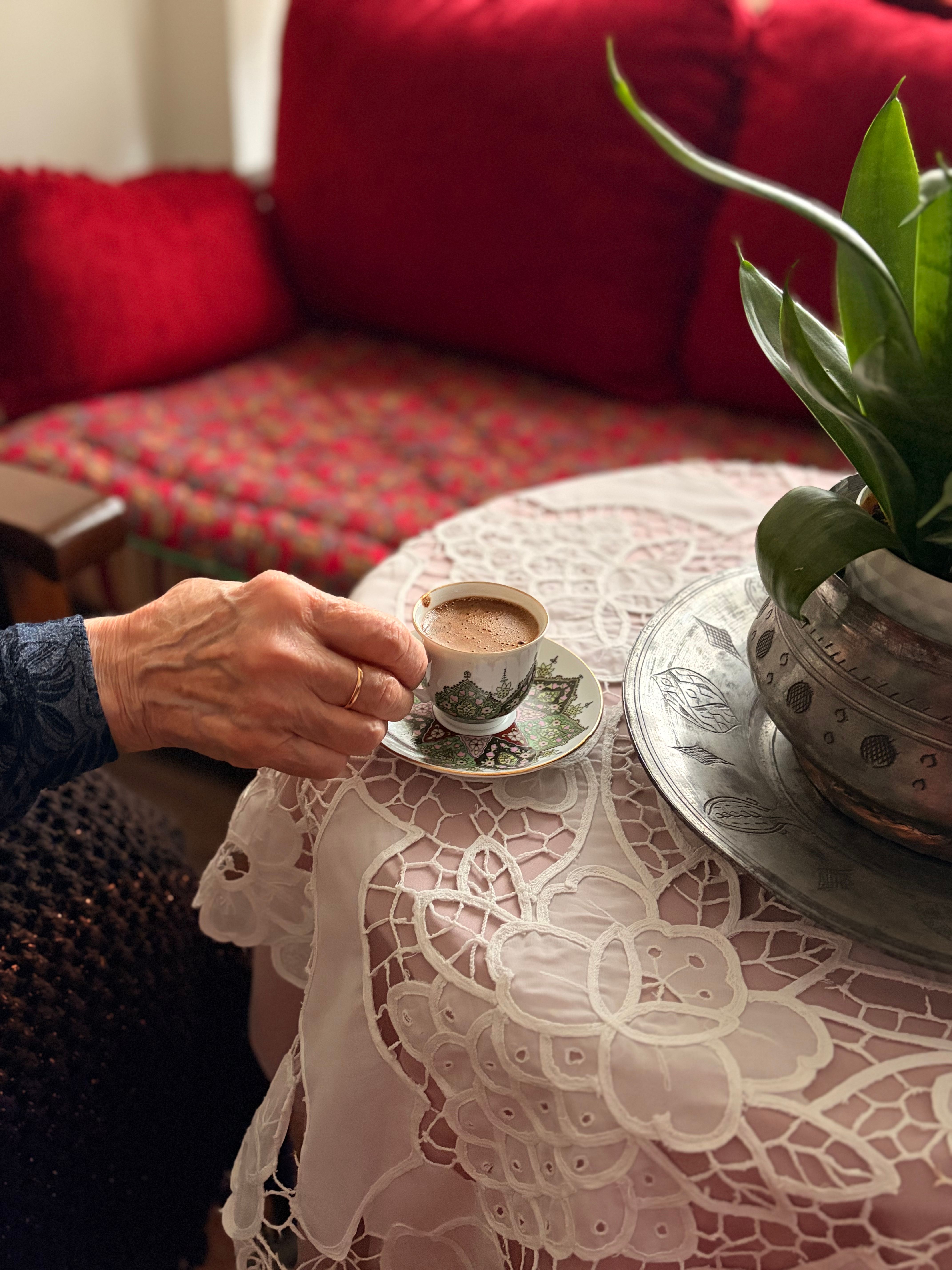A warm moment capturing a hand holding coffee on a lace-covered table indoors.