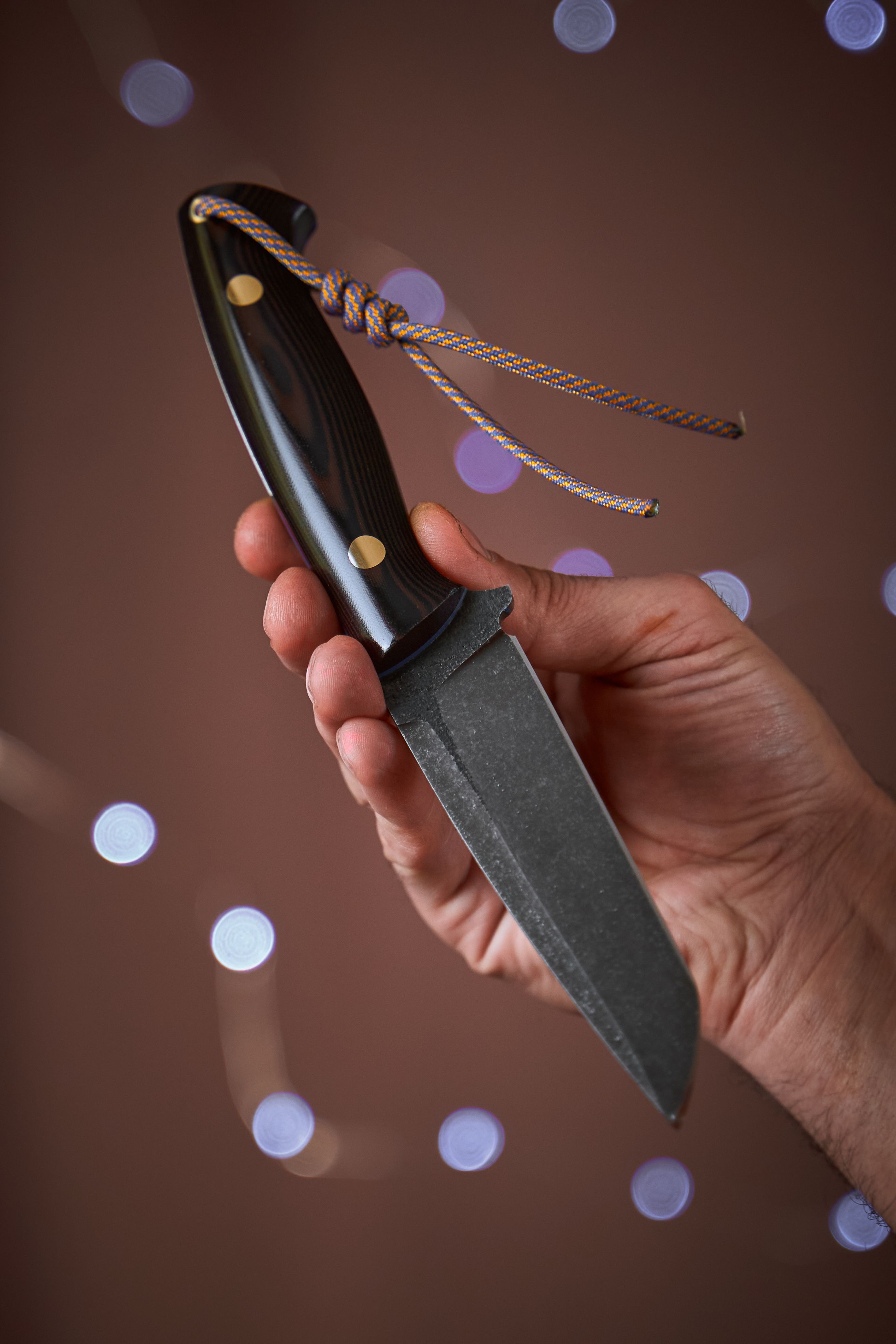 Close-up of a hand holding a custom handcrafted knife with wooden handle on a blurred background.