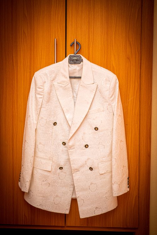 Free Classic white blazer with intricate patterns hanging on a wooden wardrobe, perfect for weddings or formal events. Stock Photo