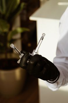 Close-up of a black-gloved hand holding syringes, signifying medical preparation.
