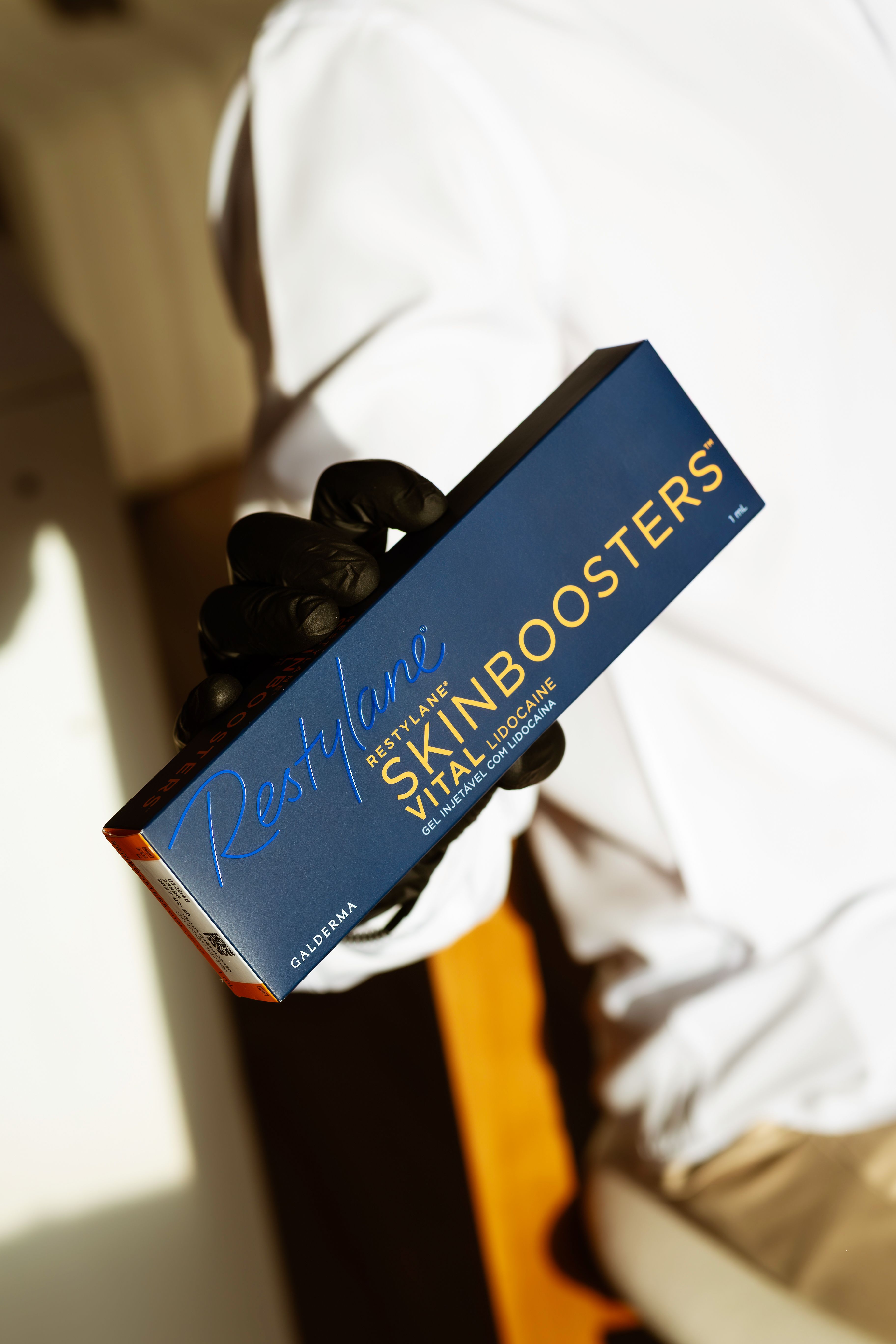 Close-up of Restylane Skinboosters box in person's hand with a black glove.