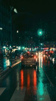 City street at night with cars and neon reflections on wet road, creating a vibrant urban atmosphere.