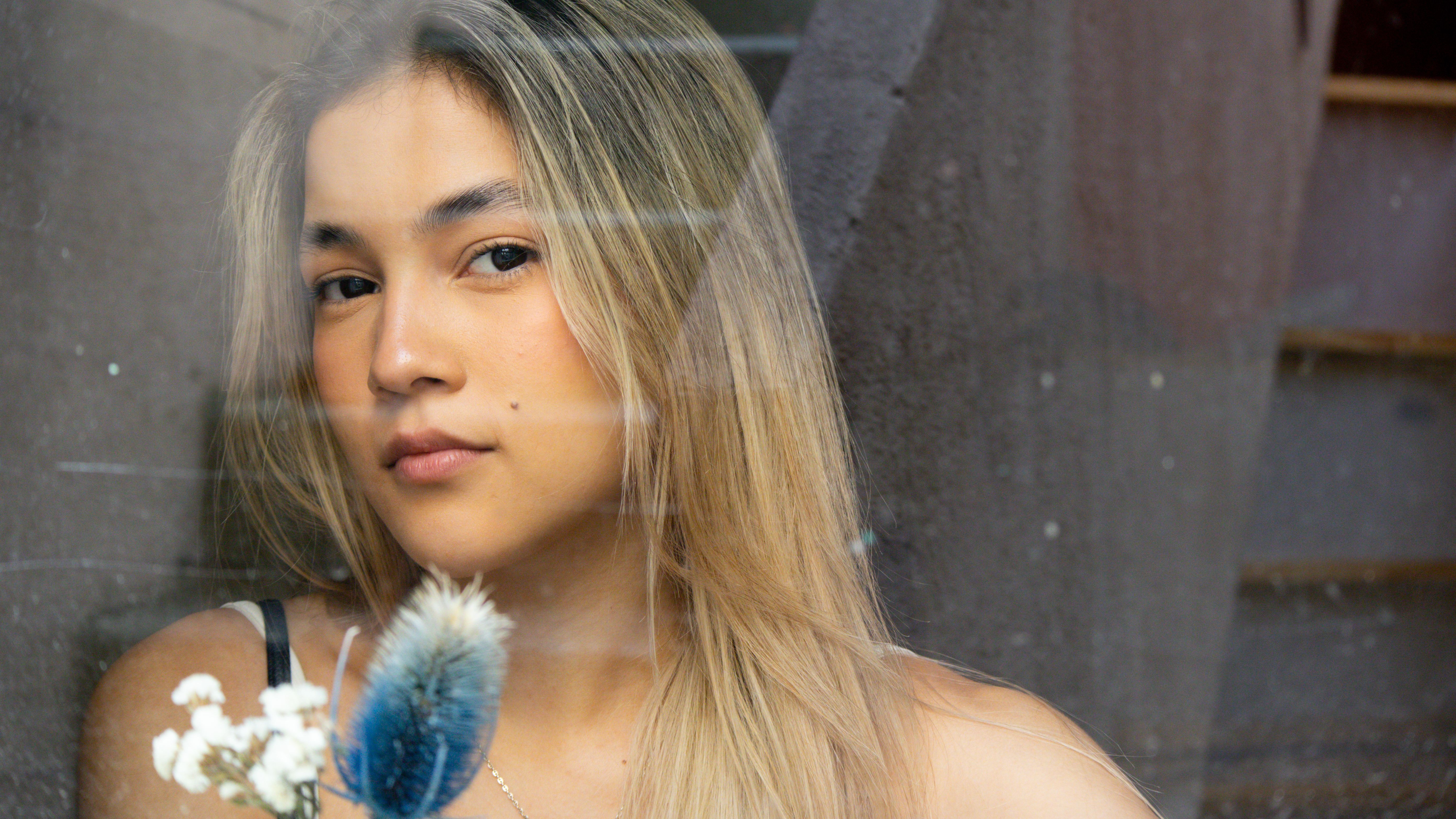 Thoughtful woman gazing through glass with decorative flowers, offering a serene mood.