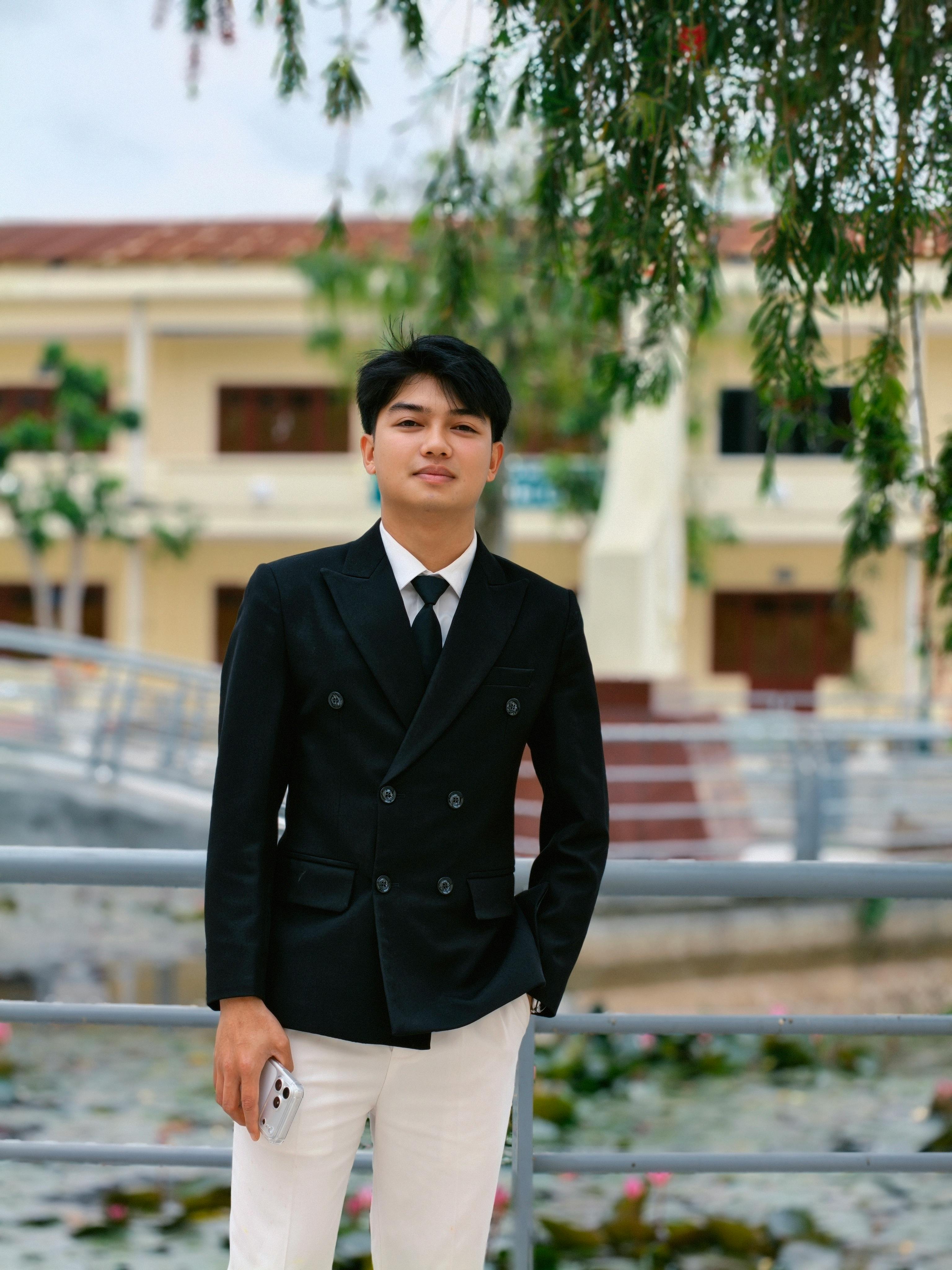 Confident young man in a black suit standing outdoors, exuding professionalism.
