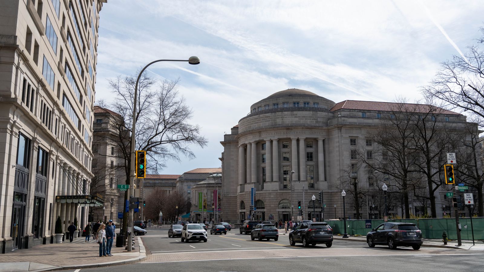 Traffic and pedestrians on a street with historic architecture in Washington DC on a clear day.