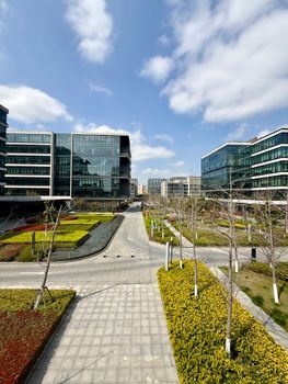 Sunny day view of a modern business park featuring glass buildings, pathways, and landscaped gardens.