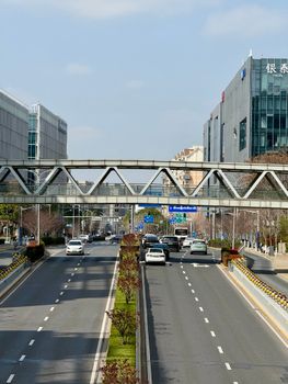 A vibrant city street with cars and a pedestrian bridge in Shanghai on a sunny day.