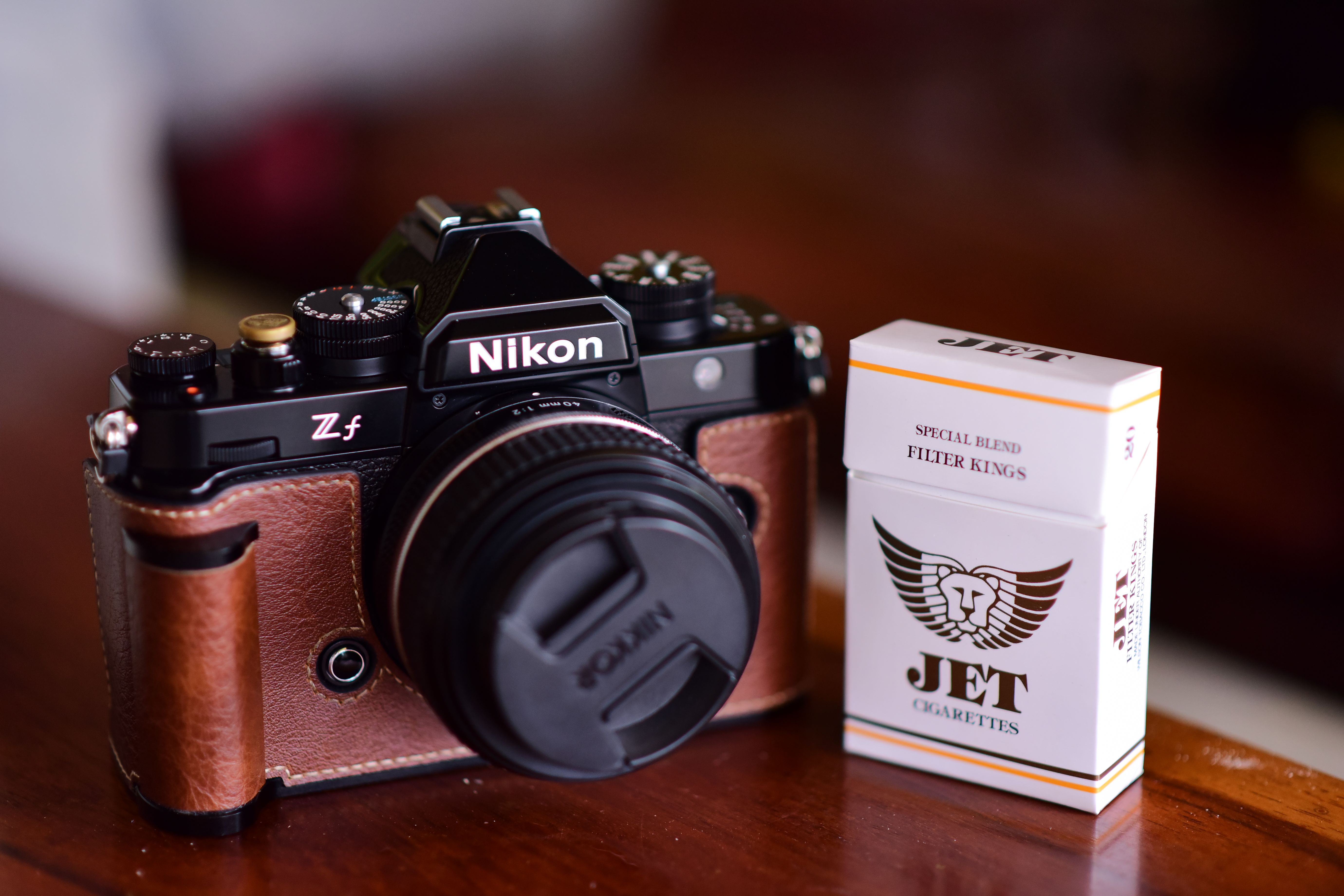 Close-up of a vintage-style camera beside a box of cigarettes on a wooden table.
