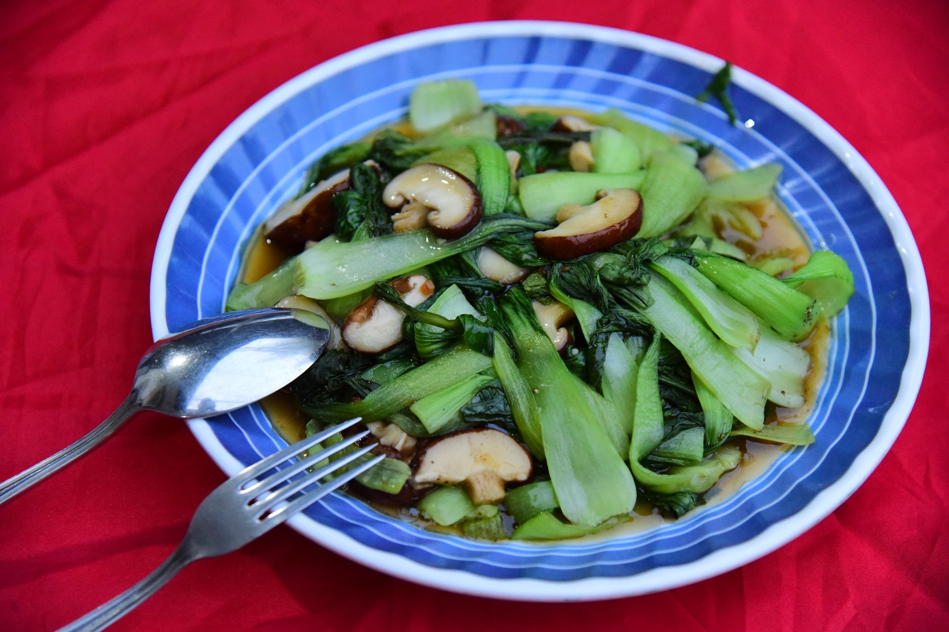 A vibrant dish of stir-fried bok choy and mushrooms served on a blue plate with red backdrop.