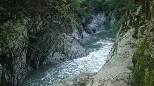 Free Serene river flanked by lush vegetation and rugged rock formations in a tranquil natural setting. Stock Photo