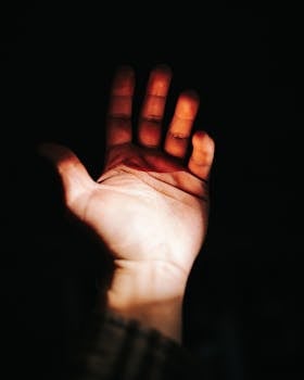 A close-up of an outstretched hand lit dramatically, emphasizing shadows and light.