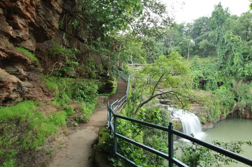 Free A serene waterfall surrounded by lush greenery and a rocky path, perfect for nature escapades. Stock Photo