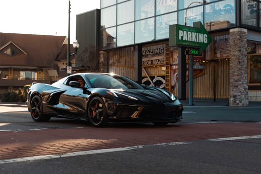 Stylish black sports car stopped at a city intersection in daylight with parking signage.