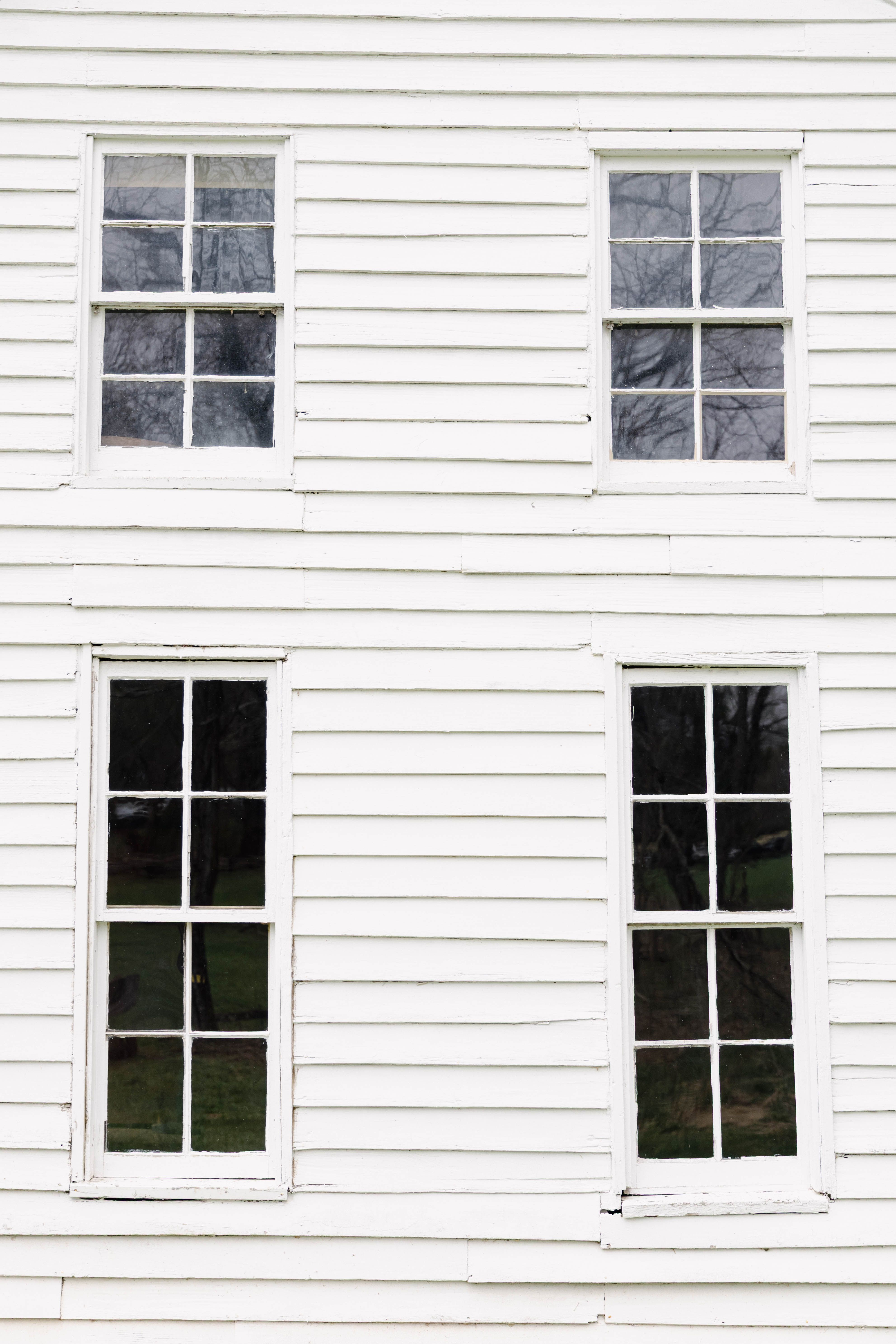 A close-up of a white wooden wall featuring four classic double-hung windows.