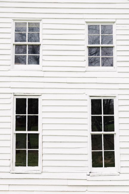 A close-up of a white wooden wall featuring four classic double-hung windows.